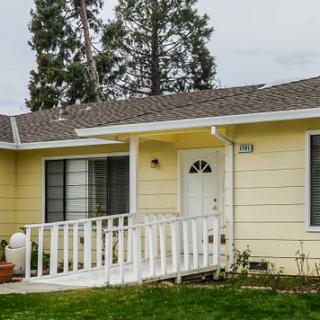 A single-story yellow house with a front entrance ramp and a green yard.