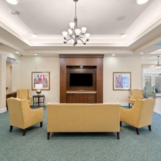 A spacious living room with yellow seating, a television, and a chandelier.
