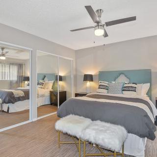 A modern bedroom with a ceiling fan, mirrored closet doors, and stylish decor.