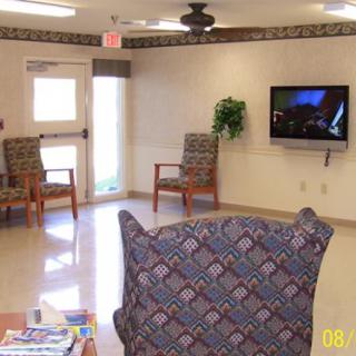 An empty waiting room with patterned chairs, a wall-mounted television, and decorative plants.