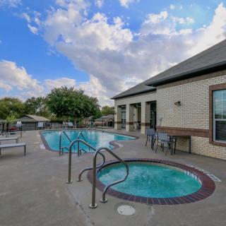 A residential outdoor area featuring a pool and jacuzzi, surrounded by patio furniture and a cloudy sky in the background.