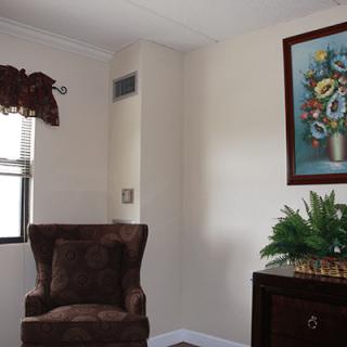 A cozy living room corner featuring an armchair, a vibrant painting, and a potted plant by the window.