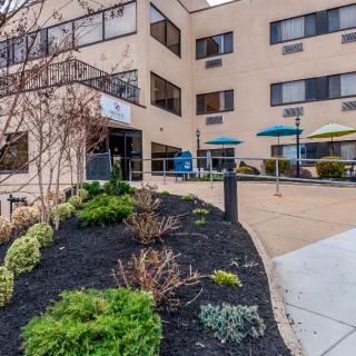 Exterior view of a building entrance with landscaping and a seating area with umbrellas.