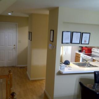A modern apartment interior featuring a view of the kitchen and adjacent hallway with wooden flooring.
