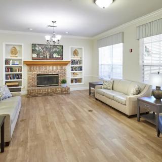 A spacious living room featuring hardwood floors, modern sofas, a central fireplace framed by bookshelves, and large windows.