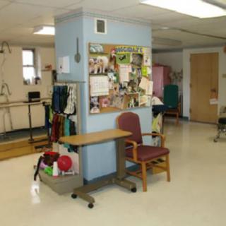 A therapy room in a healthcare facility with an office chair, bulletin board, and rehabilitation equipment.