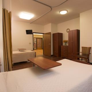 A view of a simple, well-furnished room showcasing a bed, wardrobe, television, and seating area.