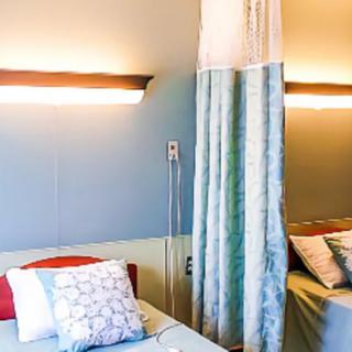 A hospital room with beds separated by a curtain and equipped with pillows.