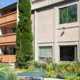 An outdoor view of an apartment building with balconies and a landscaped garden, featuring trees and plants.