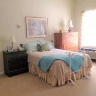 A cozy bedroom with a neatly made bed, bedside table, and chest of drawers.