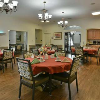 A well-arranged dining room with tables set for a meal, featuring chandeliers and wooden flooring.