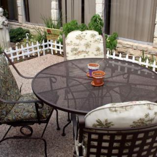 A cozy outdoor patio setting with a round metal table and cushioned chairs, adorned with small candles, surrounded by a white picket fence.