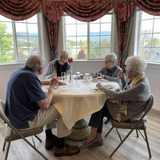 A group of elderly friends enjoying a meal together at a table with a scenic view.