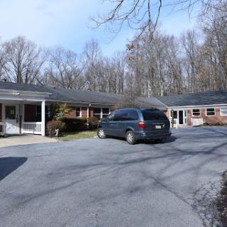 A view of a residential building with a parked car in the driveway, surrounded by trees on a clear day.