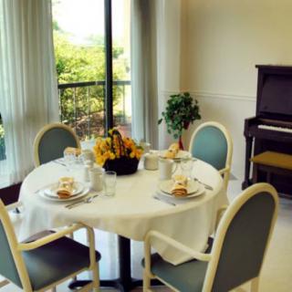 A bright and inviting dining area with a round table set for four, featuring a centerpiece of sunflowers and a piano in the background.