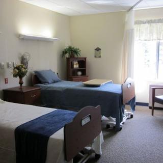 A clean and well-organized hospital room with two beds, a window, and essential furniture.