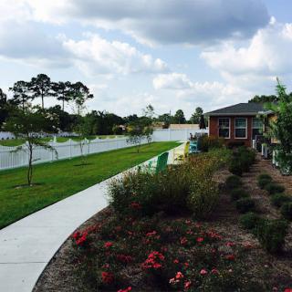 A serene view of a landscaped pathway alongside vibrant gardens and a residential building under a cloudy sky.