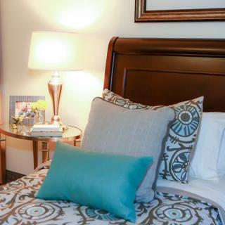A cozy bedroom setting with patterned pillows, a wooden headboard, and a lit lamp on the nightstand.