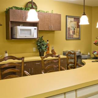 A cozy kitchen featuring warm yellow walls, wooden cabinetry, and a bar area with stools.