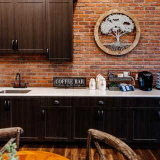 A cozy kitchen area featuring a coffee bar against a rustic brick wall with dark cabinets.