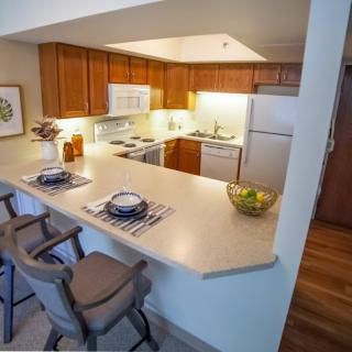 A modern kitchen with wooden cabinets and a clean countertop, featuring stools for seating.