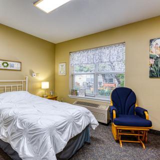 A cozy bedroom with a bed, blue chair, and large window providing natural light.