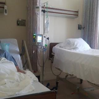 A hospital room featuring two beds with patients and medical equipment.