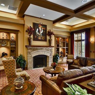 A traditionally decorated living room with a fireplace, coffered ceiling, and warm-toned furniture.