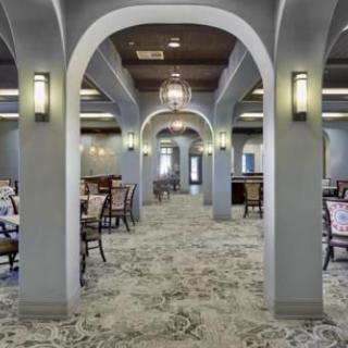 A spacious dining room featuring elegant arches, ambient lighting, and neatly arranged tables and chairs on a patterned carpet.