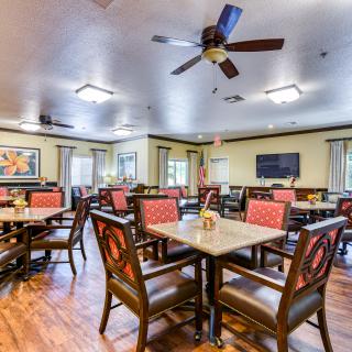 A spacious dining room with multiple tables and chairs, featuring a ceiling fan and bright lighting.