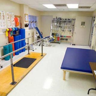 A well-equipped physical therapy room featuring parallel bars, exercise equipment, and a treatment table.