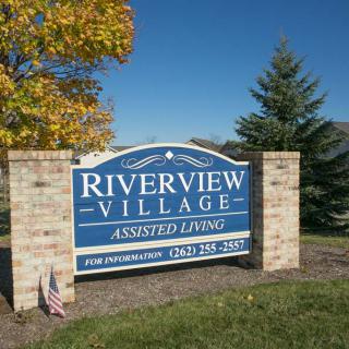 Sign for Riverview Village Assisted Living surrounded by trees and brick pillars.