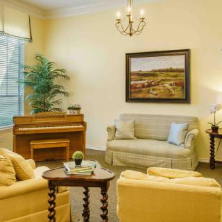 A cozy living room featuring a sofa, piano, artwork on the wall, and a chandelier.