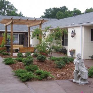 A neatly landscaped courtyard featuring a pergola, garden statue, and various plants.