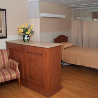 A hospital room with a bed, privacy curtain, and a vase of flowers on a counter.