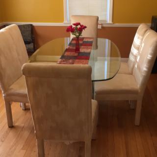A cozy dining room with a glass-top table surrounded by cushioned chairs, adorned with a floral centerpiece and warm lighting.