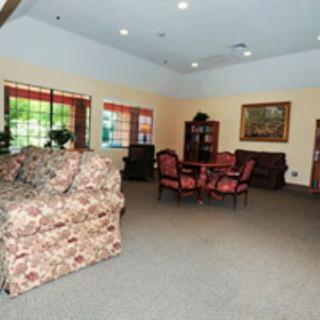 A spacious living room featuring floral-patterned sofas, a round table with chairs, and a large window.