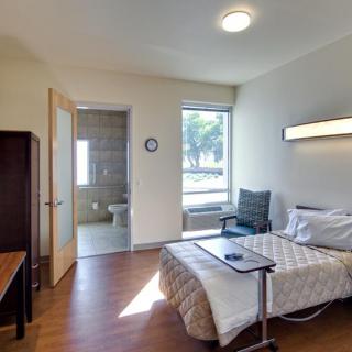 A well-lit hospital room with a bed, chair, and attached bathroom.