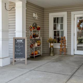A cozy porch decorated for autumn with pumpkins, a chalkboard sign, and a festive wreath on the door.