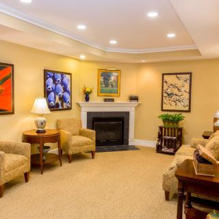 A cozy living room featuring a central fireplace, comfortable seating, and various pieces of artwork adorning the walls.