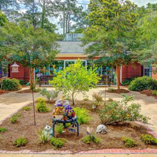 A peaceful garden scene with a sculpture on a bench and a building in the background.