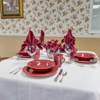 An elegantly set dining table with red dinnerware and folded napkins, accented by a floral centerpiece.