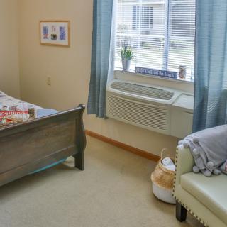 A cozy bedroom with a bed, armchair, and a window allowing natural light to fill the space.