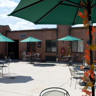 A sunny outdoor patio with tables, chairs, and umbrellas next to a brick building.