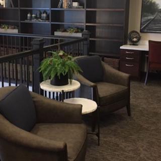 A comfortable office seating area with chairs, a plant on a side table, and shelves in the background.