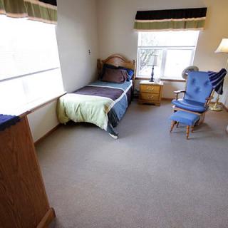 A cozy bedroom with a single bed, armchair, and wooden furniture.