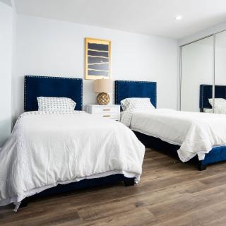A neatly arranged bedroom featuring two twin beds with blue headboards and white bedding, complemented by a nightstand and modern decor.