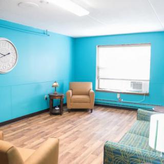 A cozy living room with blue walls, featuring two armchairs and a window letting in natural light.