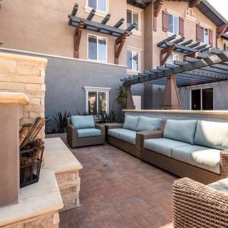 A cozy outdoor patio with comfortable sofas and a fireplace, set against a residential building.