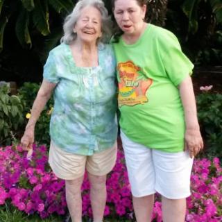 Two women standing in a garden with vibrant pink flowers.
